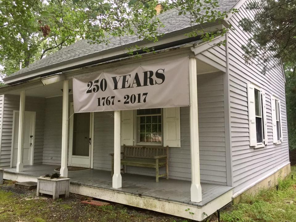 white sided bulding with large front porch and a banner proclaiming 250 years